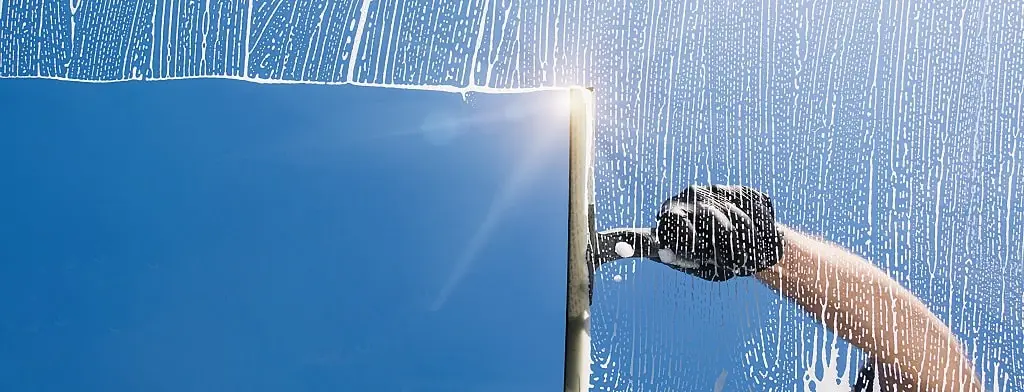 Professional squeegee cleaning a sunlit window against a bright blue sky